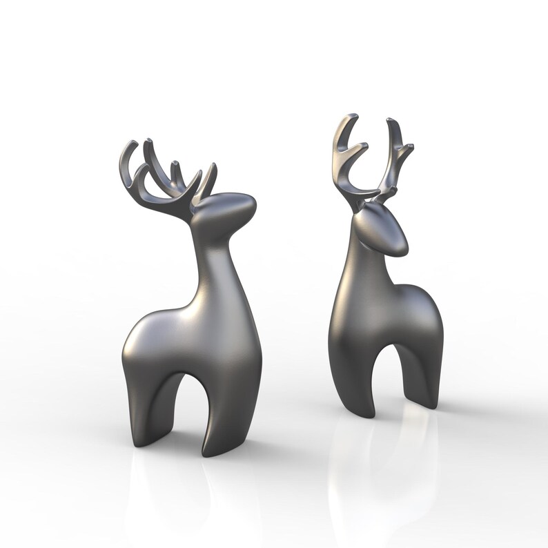 May include: Two metallic silver deer figurines. The deer have stylized bodies with arched legs and large antlers. The figurines are smooth and reflective, with a modern, minimalist design. They are set against a white background.