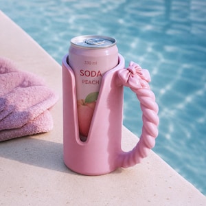 May include: A light pink beverage holder with a twisted handle and a decorative bow, containing a 330 ml soda can labeled SODA PEACH with a peach illustration. The holder features a vertical cutout design and a smooth, matte finish.