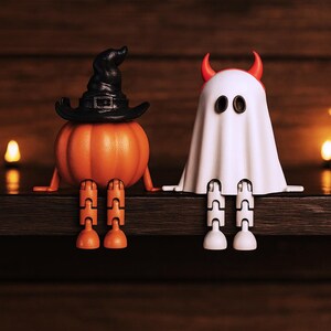 May include: Two Halloween-themed figurines sit on a wooden shelf. One is an orange pumpkin wearing a black witch hat. The other is a white ghost with red horns. Both have articulated legs and arms.
