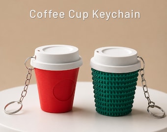 Könnte beinhalten: Zwei Kaffeetassen-Schlüsselanhänger mit weißen Deckeln und silbernen Metallringen. Eine Tasse ist einfarbig rot mit glatter Oberfläche, die andere ist dunkelgrün mit einer texturierten, gerippten Außenseite. Der Text Coffee Cup Keychain ist oben zu sehen.