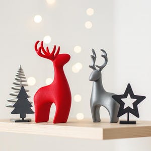 May include: A red reindeer figurine and a silver reindeer figurine stand on a wooden shelf. A black star and a black Christmas tree are also on the shelf. The background has blurred white lights.