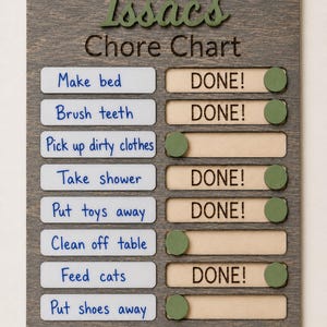 May include: A rectangular wooden chore chart with a dark grey finish. The text "Issac's Chore Chart" is at the top. Eight white horizontal labels list tasks in blue text. Each task has a sliding green wooden button to reveal the word "DONE!" in black.