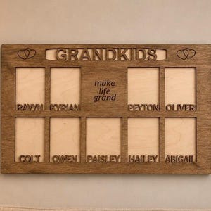 May include: A rectangular wooden photo frame with a dark brown finish featuring the word GRANDKIDS at the top, two heart icons, and the text make life grand in the center. It includes nine rectangular cutouts with names engraved below each.