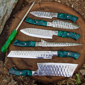 May include: A set of seven kitchen knives with green handles and a hammered finish. The knives are arranged on a wooden surface with a sharpening steel.
