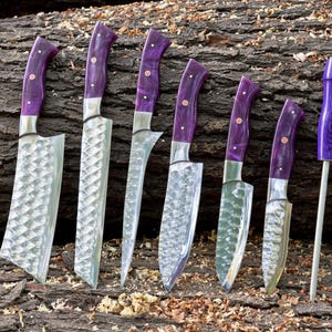 May include: A set of seven kitchen knives with purple handles and a steel sharpening steel. The knives have a hammered finish and are arranged on a wooden surface.