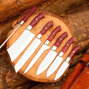 May include: Set of seven kitchen knives with red wood handles and a matching leather roll. The knives have a diamond pattern on the blades.