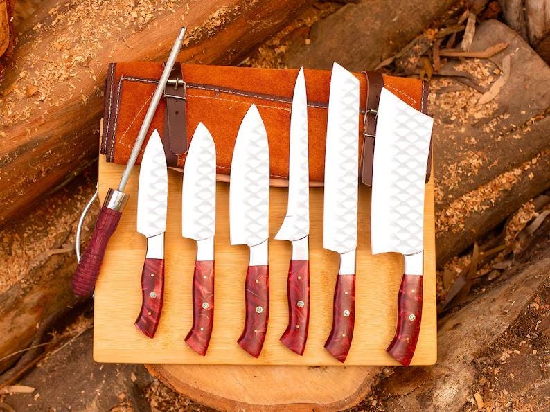 May include: Set of seven kitchen knives with red and brown handles, displayed on a wooden cutting board. The knives are arranged in a row, with the largest knife at the top and the smallest knife at the bottom. The knives are all sharp and have a diamond-shaped pattern on the blades.