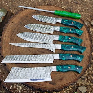 May include: Set of seven kitchen knives with green and black handles. The knives have a hammered finish and are arranged on a wooden surface.