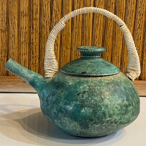 May include: A green ceramic teapot with a crackled glaze and a white rope handle.