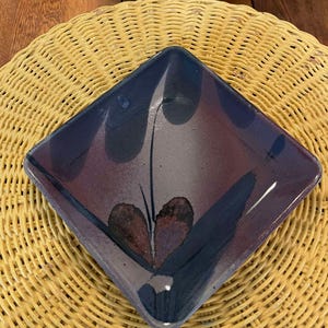 May include: Square ceramic dish with a dark blue, purple, and brown glaze. The glaze has a marbled effect with a heart-shaped design in the center.