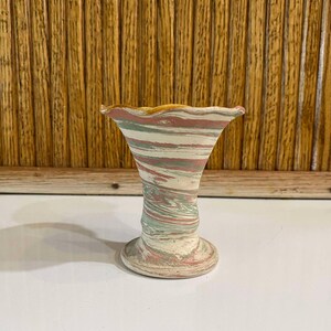 May include: A decorative ceramic vase with a flared top and a pedestal base. The vase features a swirl pattern of white, pink, and green. The rim has a yellow-orange trim. The vase is approximately 6 inches tall.
