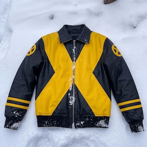 May include: A black and yellow jacket featuring a large X-shaped pattern across the front, a central zipper, a standard collar, and ribbed cuffs. The sleeves display two horizontal yellow stripes and a circular X-Men logo on each shoulder.
