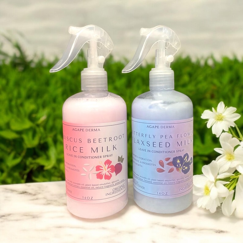 May include: Two spray bottles of Agap&eacute; Derma leave-in conditioner. One bottle is pink and labeled "Hibiscus Beetroot Rice Milk." The other is blue and labeled "Butterfly Pea Flower Flaxseed Milk." Each bottle is 14 oz. and has a white spray nozzle.