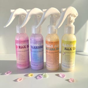 Peut inclure: Quatre flacons de vaporisateur de revitalisant sans rinçage avec des buses blanches. Les bouteilles sont étiquetées avec les noms suivants : Hibiscus Rice Milk, Butterfly Flaxseed, Peach Agave Satana Milk et Mango Milk Tea. Les bouteilles sont roses, violettes, pêche et jaunes.