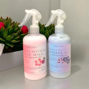 May include: Two spray bottles of Agape Derma leave-in conditioner. One is pink with hibiscus beetroot rice milk, the other is blue with butterfly pea flower flaxseed milk. Each bottle is 14 oz. and has a white spray nozzle.