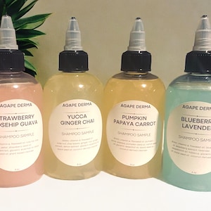 May include: Four clear plastic bottles with black caps and labels. Each bottle contains a different colored liquid and has a different scent. The labels read "Agape Derma" and list the scent of each bottle: Strawberry Rosehip Guava, Yucca Ginger Chai, Pumpkin Papaya Carrot, and Blueberry Lavender. Each bottle is labeled "Shampoo Sample".