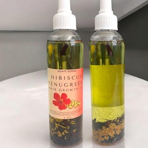 May include: Two clear glass bottles with white caps filled with a yellow liquid and red and brown flower petals and seeds. The bottles are labeled "Hibiscus Fenugreek Hair Growth Oil" and "Agape Derma". Each bottle contains 4 oz of oil.