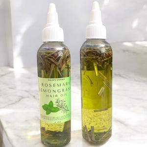May include: Two clear glass bottles with white caps filled with a green liquid and herbs. The bottles are labeled "Agape Derma Rosemary Lemongrass Hair Oil" and contain 4 oz of product.