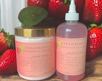 May include: Two pink bottles with gold lids and labels. The bottles are filled with a pink liquid. The labels say "Strawberry Rosehip Guava Agape Derma" and list ingredients. The bottles are sitting on a wooden surface with red strawberries in the background.