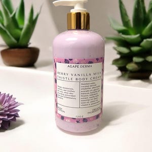 May include: A pink body lotion bottle with a white pump and gold collar. The label reads "Berry Vanilla Milk Thistle Body Cream" and lists organic ingredients. The bottle contains 12 oz of lotion.