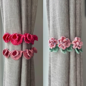 Può includere: Due set di fermagli per tende a forma di fiore all'uncinetto. Un set è rosa e l'altro è una miscela di rosa, bianco e verde.