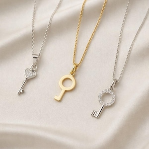 Può includere: Tre collane con ciondoli a forma di chiave in oro e argento. Una collana d'argento presenta una chiave a forma di cuore con pietre trasparenti. Il secondo è un ciondolo a forma di chiave d'oro. Il terzo è un ciondolo a forma di chiave d'argento con un cerchio di pietre trasparenti.