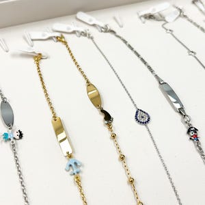 May include: A display of gold and silver children's bracelets with various charms, including a sailboat, an anchor, a heart, an evil eye, and a pirate. The bracelets are displayed on a white background.