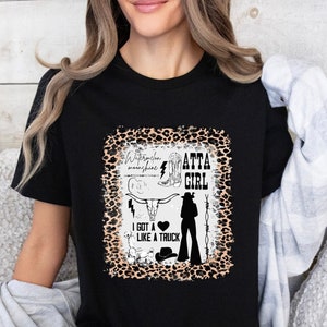 May include: Black t-shirt with a leopard print design featuring a silhouette of a woman wearing cowboy boots and a cowboy hat. The text "Watermelon sunshine Atta Girl" and "I got a heart like a truck" are printed on the shirt.