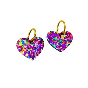Könnte beinhalten: Ein Paar goldene Creolen mit einem herzförmigen Anhänger. Die Anhänger sind aus schimmerndem Acryl und haben ein Konfetti-artiges Muster in den Farben Rosa, Lila, Blau, Grün und Gelb.