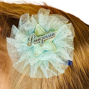 Könnte beinhalten: Eine hellblaue Tüllblumen-Haarspange mit einem glitzernden Stern und dem Wort "Prinzessin" darauf.
