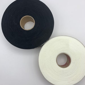 Op de afbeelding: Twee spoelen met stoffen band, een zwarte en een witte. De spoelen zijn omwikkeld met stoffen band en hebben een kartonnen kern.