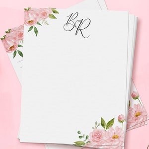 Op de afbeelding: Een stapel wit briefpapier met roze bloemenmotieven en het monogram "BR" gedrukt in zwarte inkt.