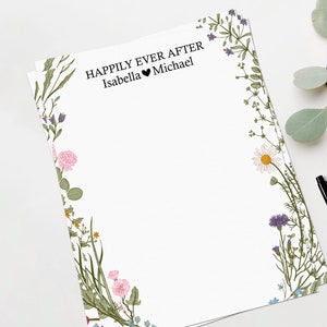 Könnte beinhalten: Weißes Briefpapier mit einem floralen Randdesign. Der Text "Happily Ever After" ist oben gedruckt, darunter die Namen "Isabella" und "Michael".