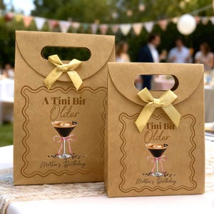May include: Two brown paper gift bags with gold bows and handles. Each bag features a decorative frame with the text "A Tini Bit Older" and a martini illustration. The text "Martin's Birthday" is also printed on the bags.