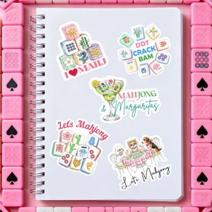 Może przedstawiać: Biały spiralny notatnik z kilkoma kolorowymi naklejkami przedstawiającymi kafelki Mahjong, koktajle oraz tekst "I ❤️ MAHJ", "Mahjong & Margaritas" i "Let's Mahjong". Naklejki otoczone są r&oacute;żowymi kafelkami Mahjong.