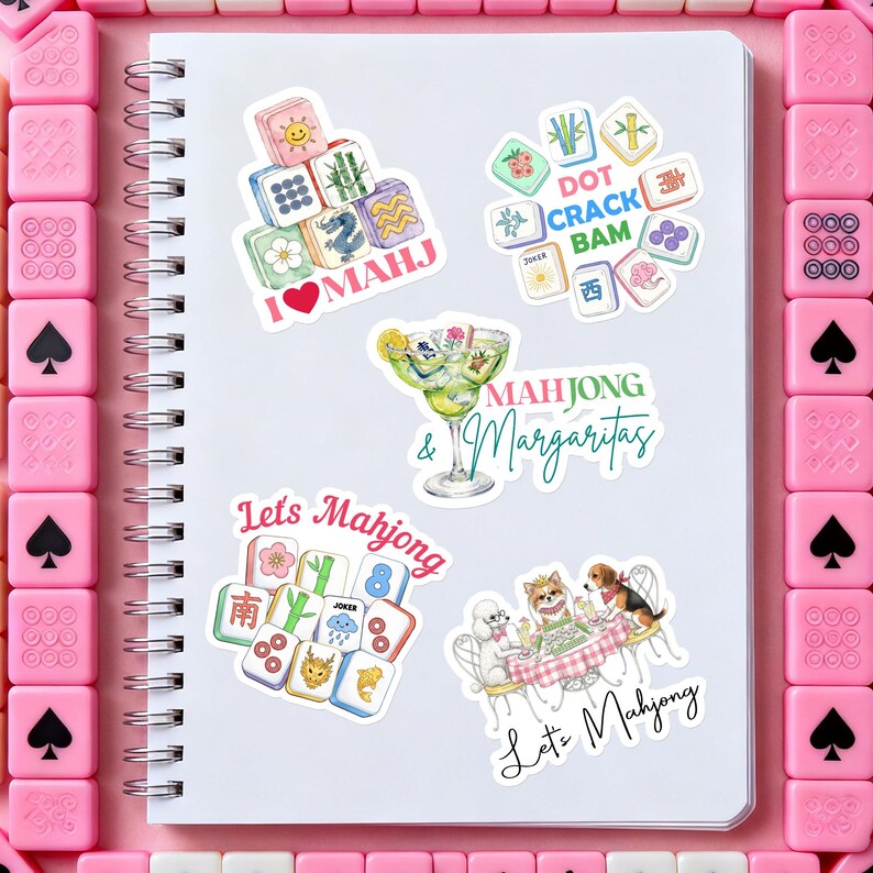 Może przedstawiać: Biały spiralny notatnik z kilkoma kolorowymi naklejkami przedstawiającymi kafelki Mahjong, koktajle oraz tekst "I ❤️ MAHJ", "Mahjong & Margaritas" i "Let's Mahjong". Naklejki otoczone są r&oacute;żowymi kafelkami Mahjong.
