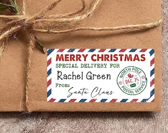 May include: A brown package tied with twine, featuring a rectangular label with the text "MERRY CHRISTMAS" and "SPECIAL DELIVERY FOR Rachel Green From: Santa Clans." The label has red, white, and blue striped borders and a North Pole Postal Service stamp.
