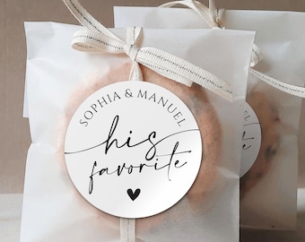 Op de afbeelding: Witte cadeautasjes met een ronde sticker waarop staat "Sophia & Manuel zijn favoriet" met een klein zwart hartje.
