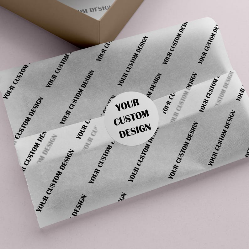 May include: White tissue paper with a repeating "YOUR CUSTOM DESIGN" pattern, wrapped around an item. A round sticker with the text "YOUR CUSTOM DESIGN" is on top. A brown box is in the background.
