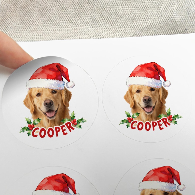 Op de afbeelding: Ronde stickers met een golden retriever met een rode kerstmuts. De naam van de hond, "COOPER", staat in rode letters onder de hond, omringd door groene hulst en rode bessen. De stickers zijn wit.