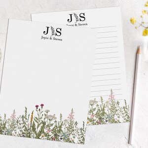 以下が含まれることがあります： 花柄の縁取りが施された白い紙が2枚。上の紙には「J.S.」のイニシャルと「Joyce & Steven」の文字が書かれている。下の紙にも「J.S.」のイニシャルと「Joyce & Steven」の文字が書かれている。紙は書き込み用に罫線が引かれている。