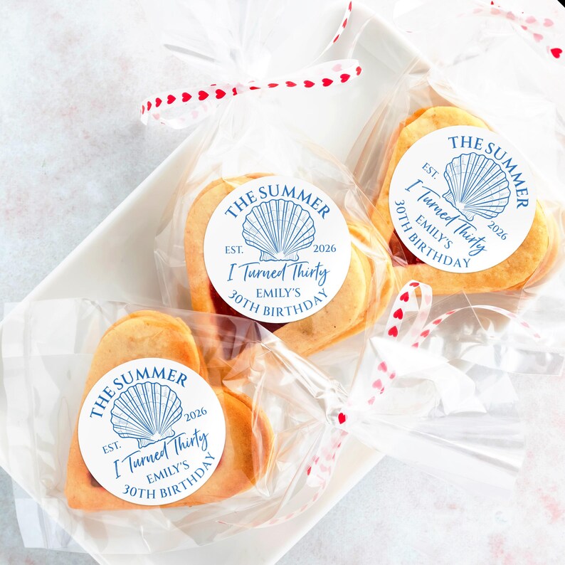 May include: Heart-shaped cookies in clear cellophane bags, tied with red and white heart-patterned ribbon. Each cookie has a white sticker with blue text that reads "The Summer, I Turned Thirty, Emily's 30th Birthday, Est. 2026" and a seashell graphic.