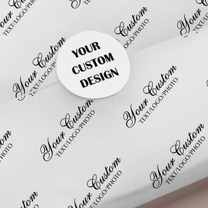 May include: White wrapping paper with a repeating pattern of the words "Your Custom TEXT/LOGO/PHOTO" in black script. A white circular sticker with the text "YOUR CUSTOM DESIGN" in bold black letters is centered on the paper.