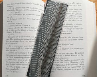 May include: A gray and white snakeskin-patterned bookmark is inserted into a book. The bookmark is rectangular with a clear plastic edge. The book pages are visible with French text.