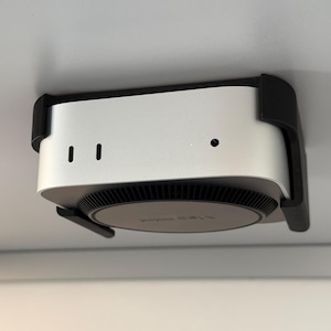 May include: A white Apple TV 4K streaming device with a black front panel and a black mounting bracket. The device is mounted to a white ceiling.