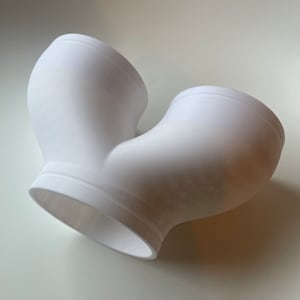 May include: A white ceramic vase with a unique U-shaped design. The vase has a smooth, rounded surface and a wide opening at the top.