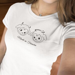 May include: White t-shirt with a graphic of two cartoon sheep, one with horns and the other with a halo. The text "Made in Heaven" is printed below the sheep.