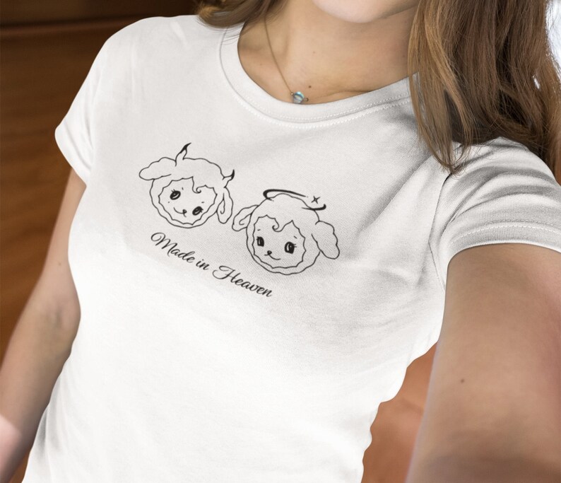 May include: White t-shirt with a graphic of two cartoon sheep, one with horns and the other with a halo. The text "Made in Heaven" is printed below the sheep.