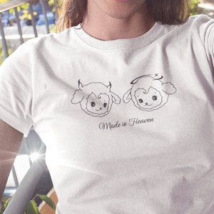 May include: White t-shirt with a graphic of two cartoon sheep, one with horns and the other with a halo. The text "Made in Heaven" is printed below the sheep.