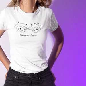 May include: White t-shirt with a graphic of two cartoon sheep, one with devil horns and the other with a halo. The text "Made in Heaven" is printed below the sheep.